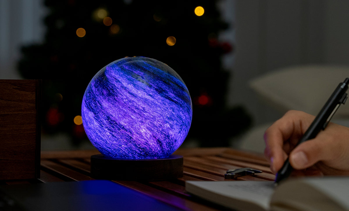 lampada AstraGlass Light. Composta da una sfera in vetro soffiata e dipinta a mano poggiata su una base rotonda in legno di noce americano. Questa lampada è perfetta per chiunque sia affascinato dal meraviglioso fenomeno naturale del nostro mondo. Dimensioni: cm ø 12 x h 13. In negozio e online su tuttochic.live