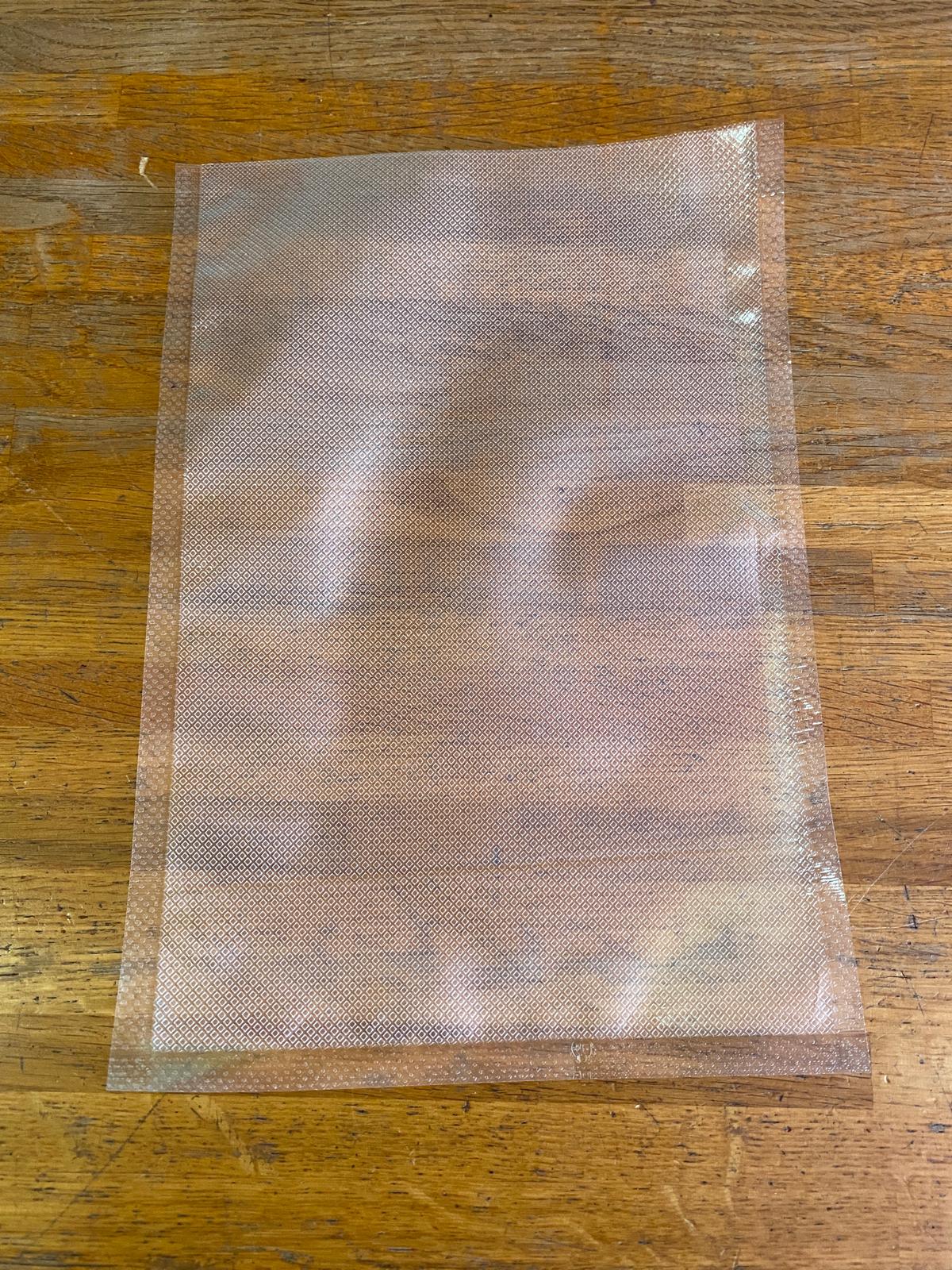 Sacchetto goffrato trasparente per cottura sottovuoto e conservazione alimenti SousVide Supreme appoggiato su piano in legno.