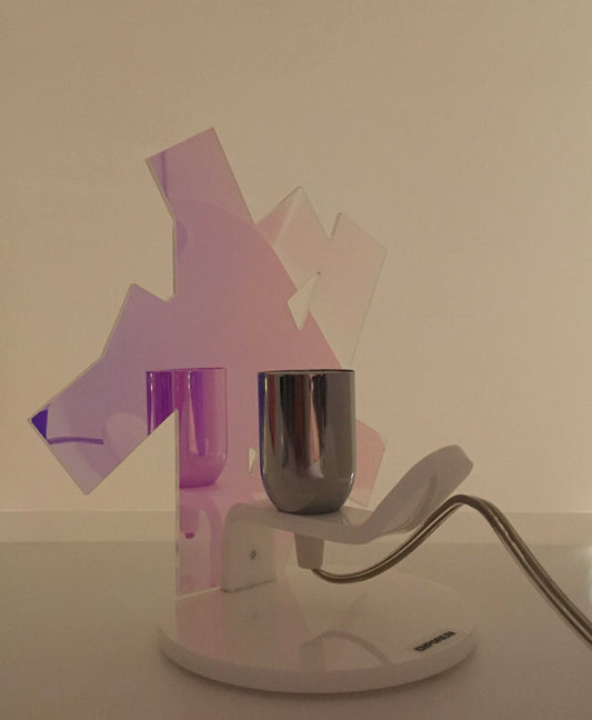 Lampada da tavolo in metacrilato dalla colorazione particolare flash (effetto specchio iridescente). Base e supporto in metacrilato bianco e portalampadina in metallo cromato. Si può applicare qualsiasi lampadina con attacco filettato E 27 (non inclusa). Dimensioni: cm 23 x 23 x 15 p. In negozio e online su tuttochic.live