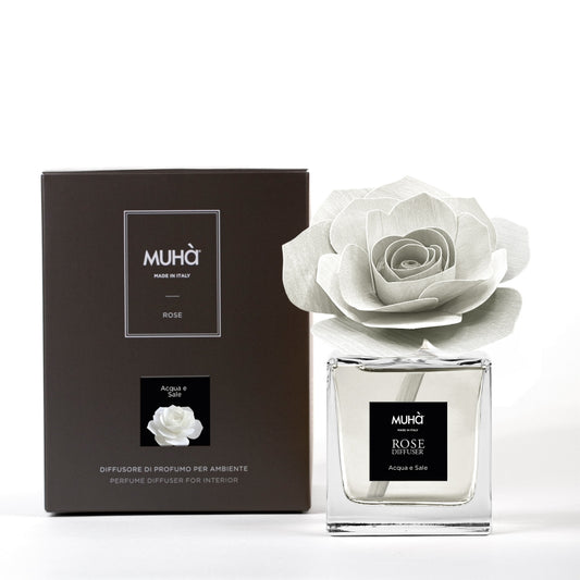 Profumatore d'ambiente Muhà Rose Diffuser Acqua e Sale in flacone squadrato di vetro trasparente con essenza cristallina, etichetta centrale quadrata nera e diffusore artigianale a forma di rosa in legno bianco avorio, Tutto Chic.
