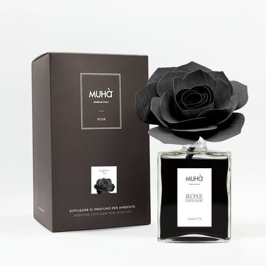 Profumatore d'ambiente Muhà Rose Diffuser Legni e Tè in flacone grande squadrato di vetro trasparente con essenza nera, etichetta verticale bianca e diffusore artigianale a forma di rosa in legno nero pece, Tutto Chic.
