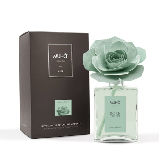 Profumatore d'ambiente Muhà Rose Diffuser Cuoio e Frutti in flacone grande squadrato di vetro trasparente con essenza verde chiaro, etichetta verticale verde salvia e diffusore artigianale a forma di rosa in legno color verde menta pallido, Tutto Chic.