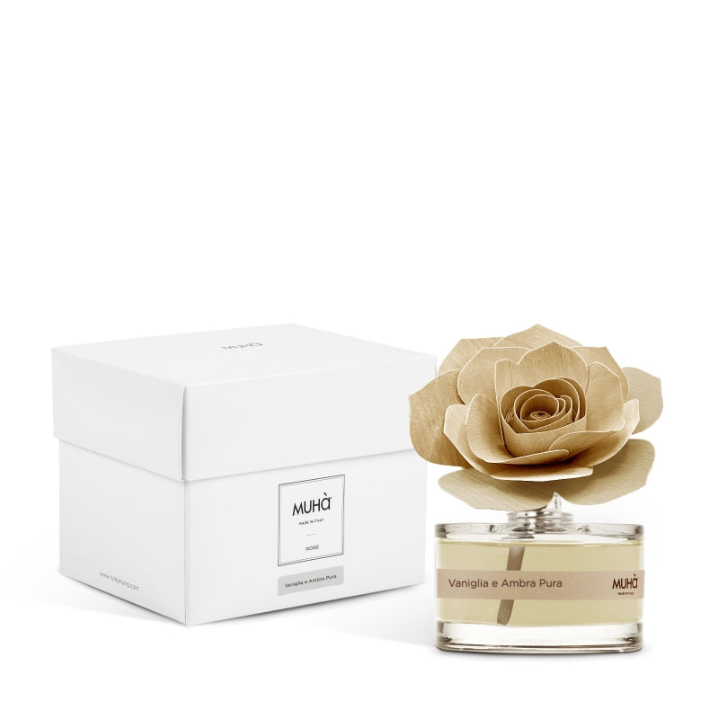 Profumatore d'ambiente Muhà Rosa Diffuser Vaniglia e Ambra Pura in boccetta di vetro trasparente con essenza dorata, etichetta beige e diffusore artigianale a forma di rosa in legno ocra chiaro, Tutto Chic.