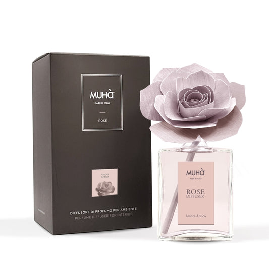 Profumatore d'ambiente Muhà Rose Diffuser Ambra Antica in flacone grande squadrato di vetro trasparente con essenza rosata, etichetta verticale rosa cipria e diffusore artigianale a forma di rosa in legno color rosa antico desaturato, Tutto Chic.