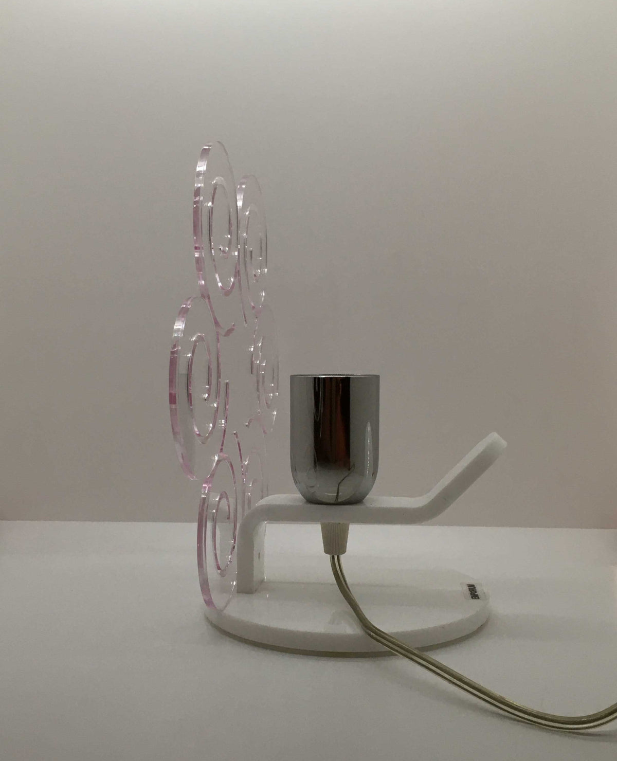 Lampada da tavolo in metacrilato trasparente con profilo viola soft. Base e supporto in metacrilato bianco e portalampadina in metallo cromato. Si può applicare qualsiasi lampadina con attacco filettato E 27 (non inclusa). Dimensioni: cm 23 x 23 x 15 p. In negozio e online su tuttochic.live