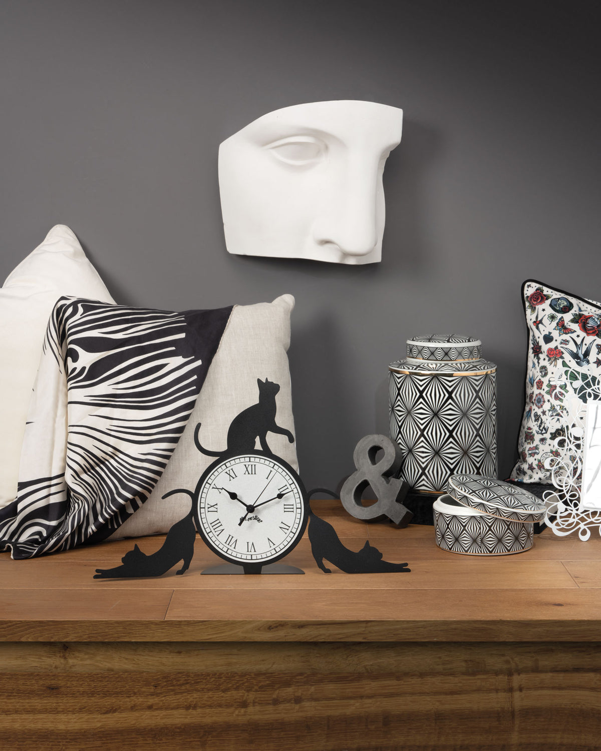 Orologio simpatico Cattitude da tavolo, realizzato in ferro e di colore nero, il complemento d’arredo originale e simpatico da collocare in una scrivania dello studio oppure sul comodino di una camera rappresenta l’allegria e la freschezza degli ambienti. Dimensioni: 48 X 30H cm. In negozio e online su tuttochic.live