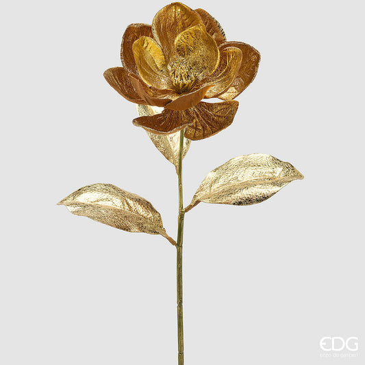 Elegante fiore singolo di magnolia artificiale alto 74 cm color oro metallizzato con due grandi foglie dorate su sfondo chiaro, firmato EDG.