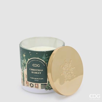 Candela natalizia profumata EDG in bicchiere di vetro verde decorato "Christmas Hamlet", con cera bianca e coperchio in metallo dorato lucido appoggiato a fianco con fiocco di neve inciso.