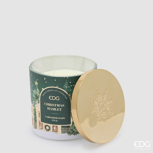 Candela natalizia profumata EDG in bicchiere di vetro verde decorato "Christmas Hamlet", con cera bianca e coperchio in metallo dorato lucido appoggiato a fianco con fiocco di neve inciso.