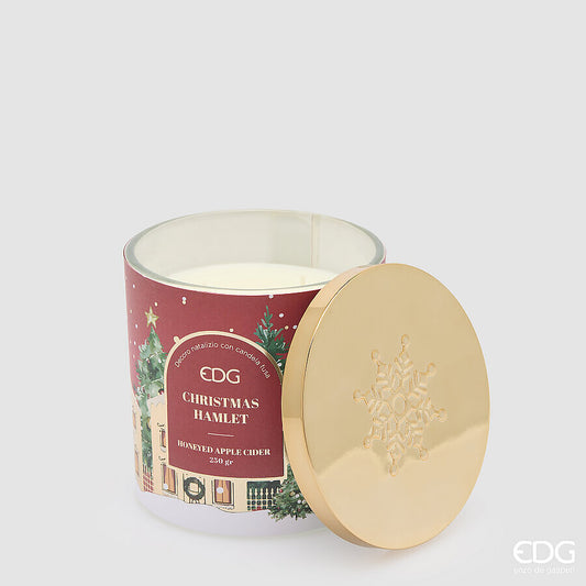 Candela natalizia profumata EDG in grande bicchiere rosso satinato decorato "Christmas Hamlet", con cera bianca e coperchio lucido in metallo dorato con fiocco di neve a rilievo.