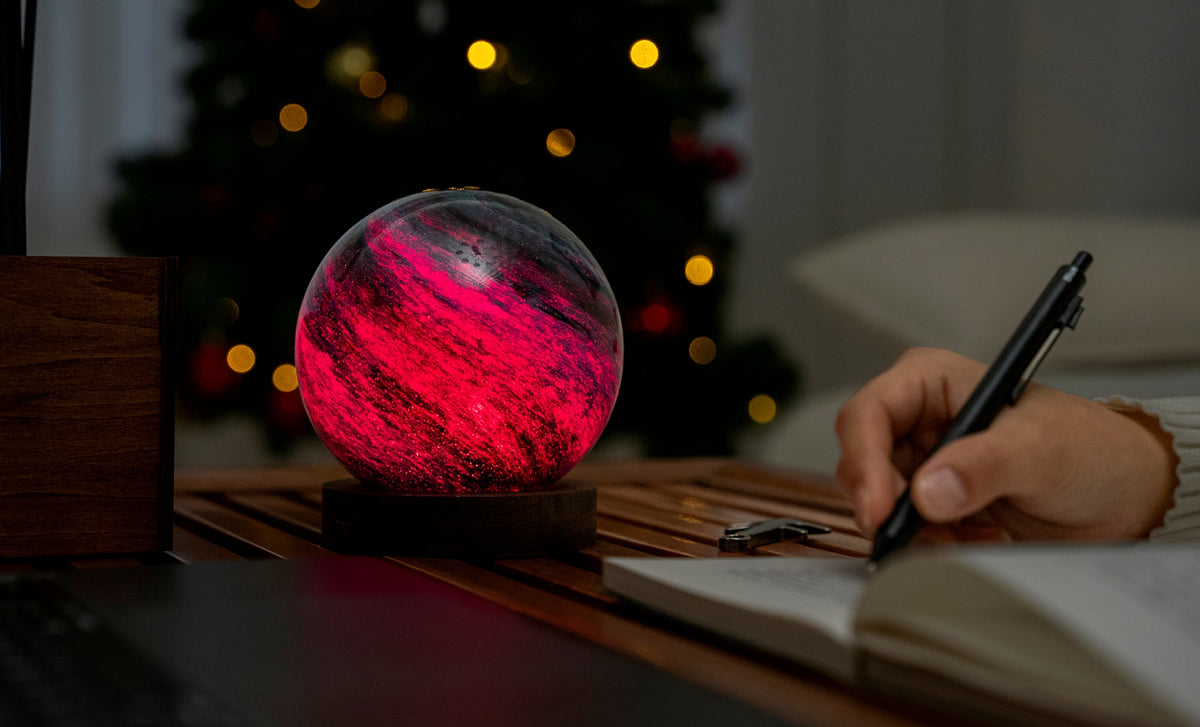 lampada AstraGlass Light. Composta da una sfera in vetro soffiata e dipinta a mano poggiata su una base rotonda in legno di noce americano. Questa lampada è perfetta per chiunque sia affascinato dal meraviglioso fenomeno naturale del nostro mondo. Dimensioni: cm ø 12 x h 13. In negozio e online su tuttochic.live
