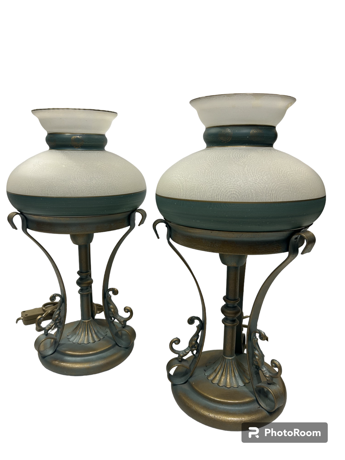 Set di 2 lampade in stile classico in metallo di colore oro e verde (effetto verderame), coppe in vetro sabbiato decorate a mano. Corredate di cavo con interruttore, funzionano con una lampadina attacco piccolo E14 (non incluse). Dimensioni: cm 18 x 35 h - base cm 14. In negozio e online su tuttochic.live