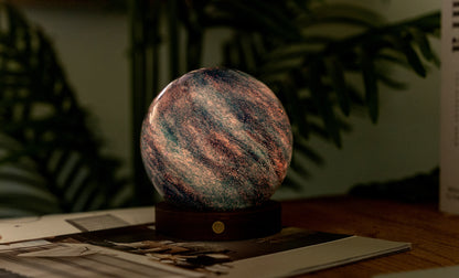 lampada AstraGlass Light. Composta da una sfera in vetro soffiata e dipinta a mano poggiata su una base rotonda in legno di noce americano. Questa lampada è perfetta per chiunque sia affascinato dal meraviglioso fenomeno naturale del nostro mondo. Dimensioni: cm ø 12 x h 13. In negozio e online su tuttochic.live