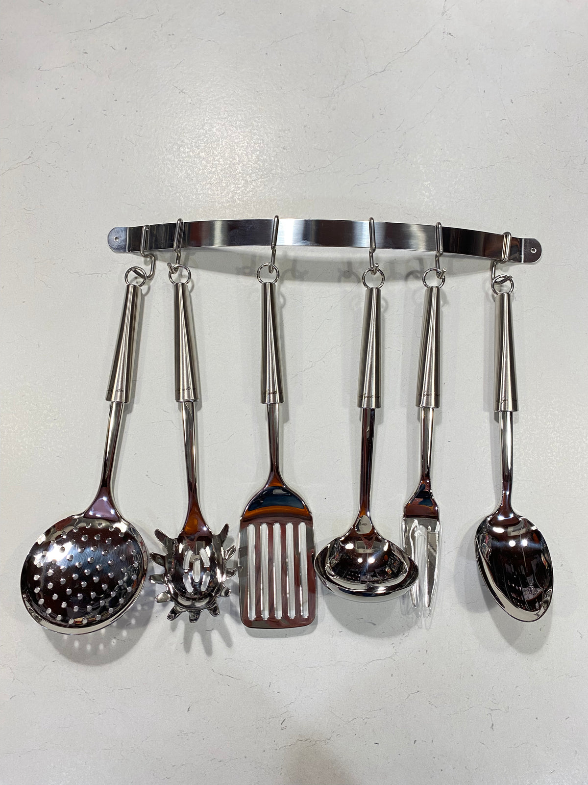 Set di 7 pezzi in acciaio inox composto da 1 Cucchiaione, 1 Forchettone, 1 Mestolo, 1 Paletta, 1 Servispaghetti, 1 Schiumarola e 1 Appendimestoli da parete (corredato di 2 tasselli). Dimensioni: cm 43 x 39 h. In negozio e online su tuttochic.live