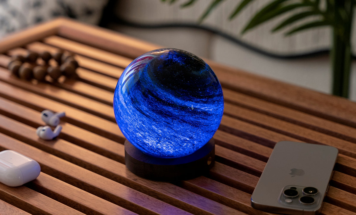 lampada AstraGlass Light. Composta da una sfera in vetro soffiata e dipinta a mano poggiata su una base rotonda in legno di noce americano. Questa lampada è perfetta per chiunque sia affascinato dal meraviglioso fenomeno naturale del nostro mondo. Dimensioni: cm ø 8 x h 9. In negozio e online su tuttochic.live