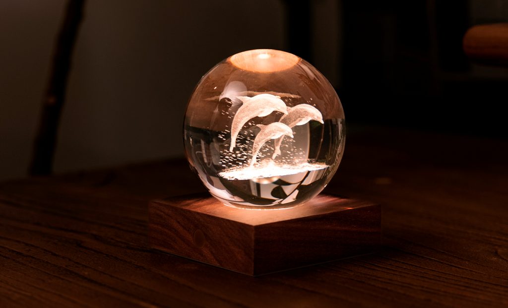 La lampada composta da una sfera in cristallo con decoro interno inciso al laser in 3D su una base quadrata in legno massello di noce naturale. Dimensioni: cm 8 x 8 x h 9,. In negozio e online su tuttochic.live