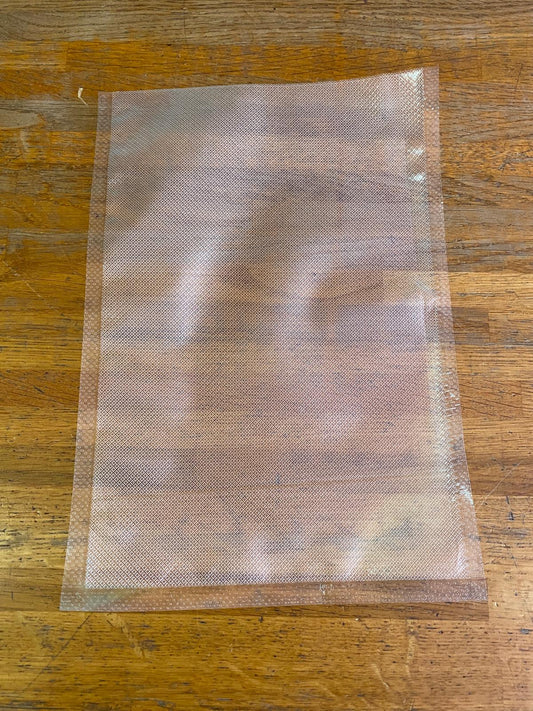 Sacchetto goffrato trasparente per cottura sottovuoto e conservazione alimenti SousVide Supreme appoggiato su piano in legno.