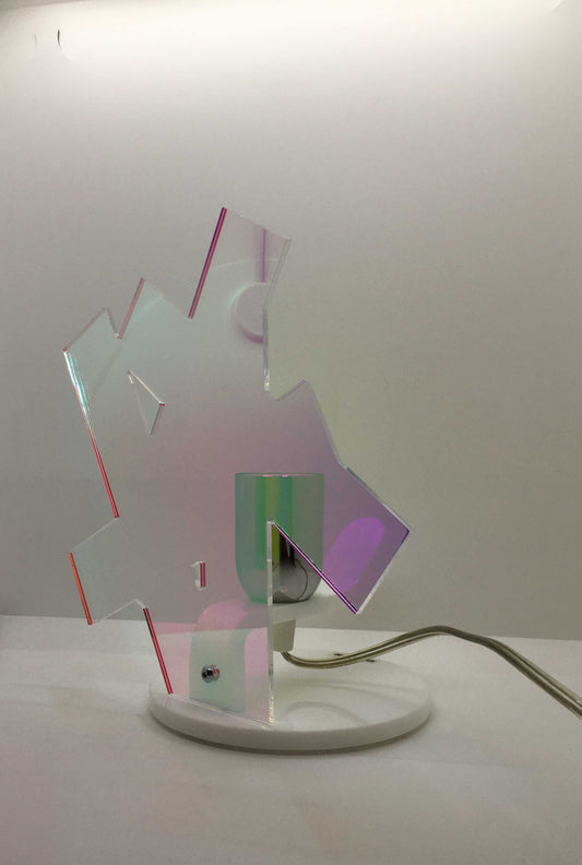 Lampada da tavolo in metacrilato dalla colorazione particolare flash (effetto specchio iridescente). Base e supporto in metacrilato bianco e portalampadina in metallo cromato. Si può applicare qualsiasi lampadina con attacco filettato E 27 (non inclusa). Dimensioni: cm 23 x 23 x 15 p. In negozio e online su tuttochic.live