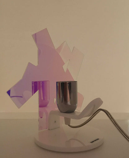 Lampada da tavolo in metacrilato dalla colorazione particolare flash (effetto specchio iridescente). Base e supporto in metacrilato bianco e portalampadina in metallo cromato. Si può applicare qualsiasi lampadina con attacco filettato E 27 (non inclusa). Dimensioni: cm 23 x 23 x 15 p. In negozio e online su tuttochic.live