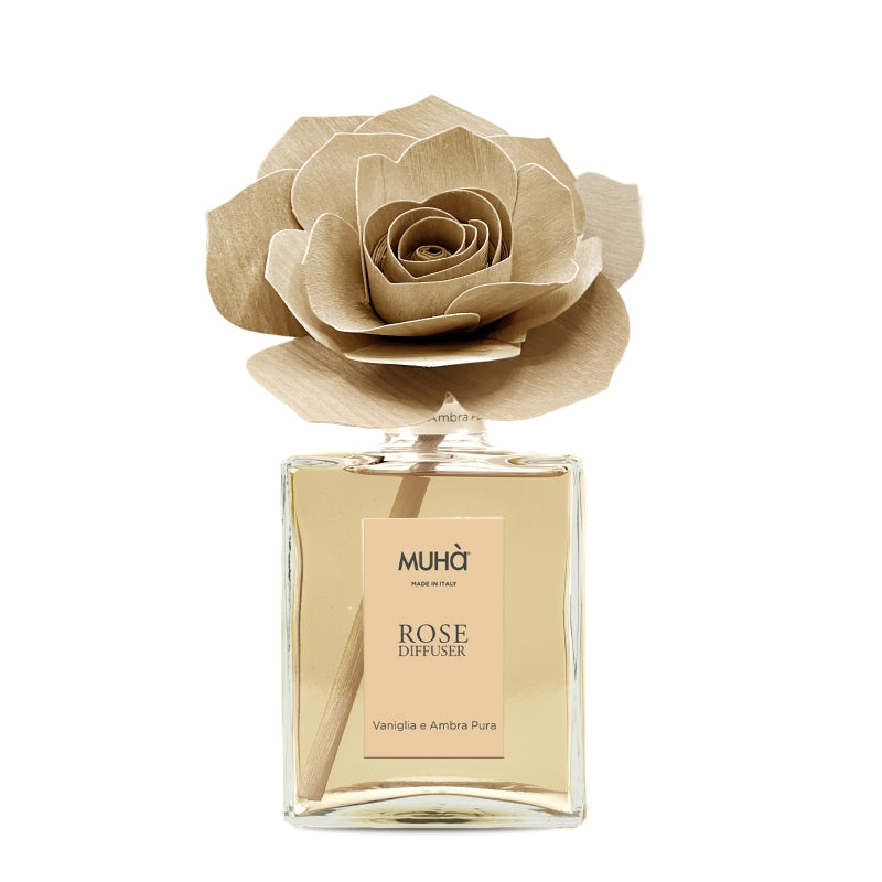 Profumatore d'ambiente Muhà Rose Diffuser Vaniglia e Ambra pura in flacone grande squadrato di vetro trasparente con essenza dorata, etichetta verticale ambra chiaro e diffusore artigianale a forma di rosa in legno color ocra tenue, Tutto Chic.