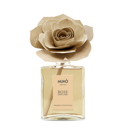 Profumatore d'ambiente Muhà Rose Diffuser Vaniglia e Ambra pura in flacone grande squadrato di vetro trasparente con essenza dorata, etichetta verticale ambra chiaro e diffusore artigianale a forma di rosa in legno color ocra tenue, Tutto Chic.