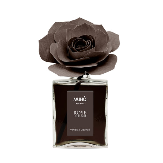 Profumatore d'ambiente Muhà Rose Diffuser Vaniglia e Liquirizia in flacone grande squadrato di vetro trasparente con essenza scura, etichetta verticale marrone e diffusore artigianale a forma di rosa in legno color cioccolato fondente, Tutto Chic.