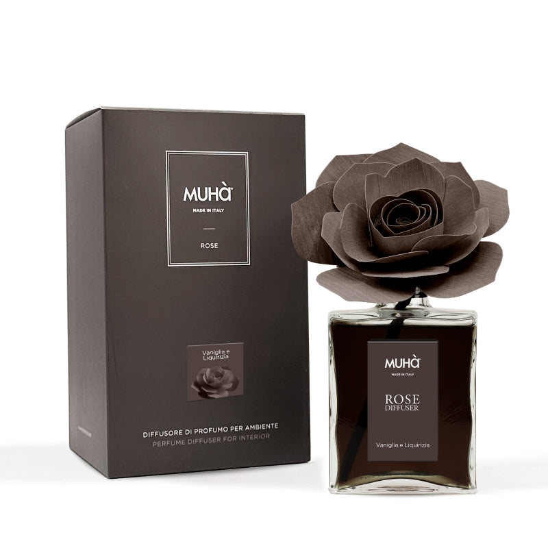 Profumatore d'ambiente Muhà Rose Diffuser Vaniglia e Liquirizia in flacone grande squadrato di vetro trasparente con essenza scura, etichetta verticale marrone e diffusore artigianale a forma di rosa in legno color cioccolato fondente, Tutto Chic.