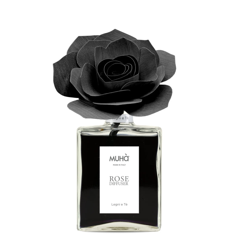 Profumatore d'ambiente Muhà Rose Diffuser Legni e Tè in flacone grande squadrato di vetro trasparente con essenza nera, etichetta verticale bianca e diffusore artigianale a forma di rosa in legno nero pece, Tutto Chic.