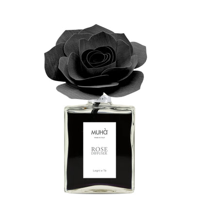 Profumatore d'ambiente Muhà Rose Diffuser Legni e Tè in flacone grande squadrato di vetro trasparente con essenza nera, etichetta verticale bianca e diffusore artigianale a forma di rosa in legno nero pece, Tutto Chic.