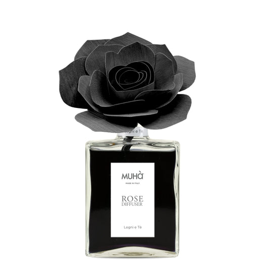 Profumatore d'ambiente Muhà Rose Diffuser Legni e Tè in flacone grande squadrato di vetro trasparente con essenza nera, etichetta verticale bianca e diffusore artigianale a forma di rosa in legno nero pece, Tutto Chic.