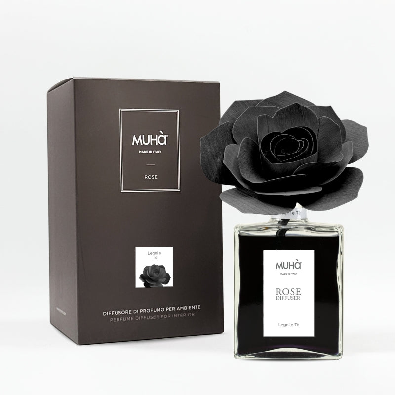 Profumatore d'ambiente Muhà Rose Diffuser Legni e Tè in flacone grande squadrato di vetro trasparente con essenza nera, etichetta verticale bianca e diffusore artigianale a forma di rosa in legno nero pece, Tutto Chic.