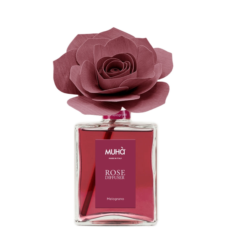 rofumatore d'ambiente Muhà Rose Diffuser Melograno in flacone grande squadrato di vetro trasparente con essenza rossa, etichetta verticale bordeaux e diffusore artigianale a forma di rosa in legno color rosso rubino profondo, Tutto Chic.