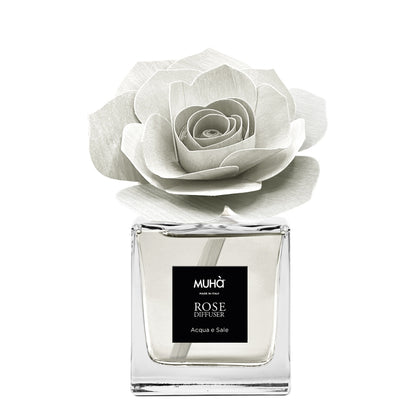Profumatore d'ambiente Muhà Rose Diffuser Acqua e Sale in flacone squadrato di vetro trasparente con essenza cristallina, etichetta centrale quadrata nera e diffusore artigianale a forma di rosa in legno bianco avorio, Tutto Chic.