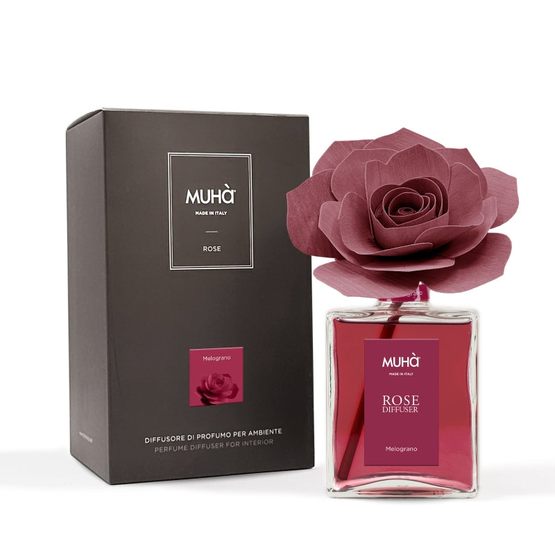 rofumatore d'ambiente Muhà Rose Diffuser Melograno in flacone grande squadrato di vetro trasparente con essenza rossa, etichetta verticale bordeaux e diffusore artigianale a forma di rosa in legno color rosso rubino profondo, Tutto Chic.