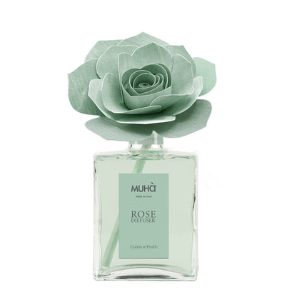 Profumatore d'ambiente Muhà Rose Diffuser Cuoio e Frutti in flacone grande squadrato di vetro trasparente con essenza verde chiaro, etichetta verticale verde salvia e diffusore artigianale a forma di rosa in legno color verde menta pallido, Tutto Chic.