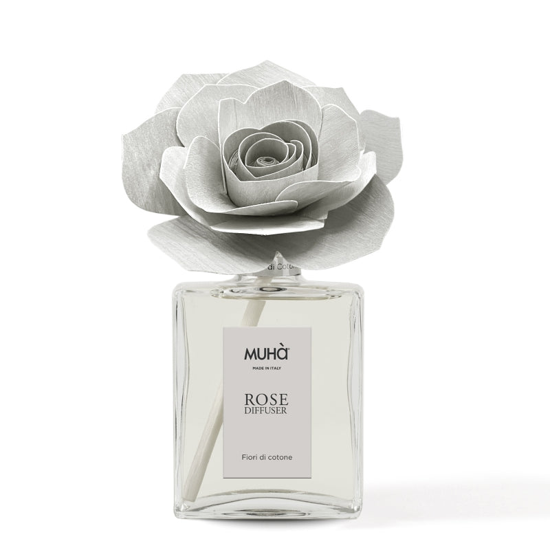Profumatore d'ambiente Muhà Rose Diffuser Fiori di Cotone in flacone grande squadrato di vetro trasparente con essenza limpida, etichetta verticale grigio perla e diffusore artigianale a forma di rosa in legno color grigio chiarissimo desaturato, Tutto Chic.