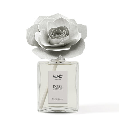 Profumatore d'ambiente Muhà Rose Diffuser Fiori di Cotone in flacone grande squadrato di vetro trasparente con essenza limpida, etichetta verticale grigio perla e diffusore artigianale a forma di rosa in legno color grigio chiarissimo desaturato, Tutto Chic.