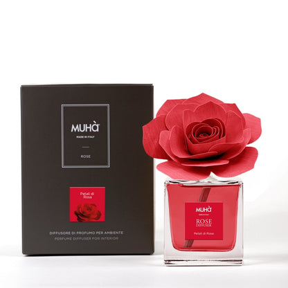 Profumatore d'ambiente Muhà Rose Diffuser Petali di Rosa in flacone squadrato di vetro trasparente con essenza rossa, etichetta quadrata centrale e diffusore artigianale a forma di rosa in legno rosso corallo vivo, Tutto Chic.