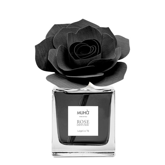 Profumatore d'ambiente Muhà Rose Diffuser Legni e Tè in flacone squadrato di vetro trasparente con essenza nera, etichetta quadrata centrale e diffusore artigianale a forma di rosa in legno nero antracite, Tutto Chic.