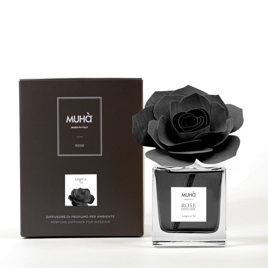 Profumatore d'ambiente Muhà Rose Diffuser Legni e Tè in flacone squadrato di vetro trasparente con essenza nera, etichetta quadrata centrale e diffusore artigianale a forma di rosa in legno nero antracite, Tutto Chic.