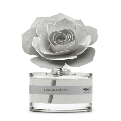 Profumatore d'ambiente Muhà Rosa Diffuser Fiori di Cotone in boccetta di vetro trasparente con essenza grigio chiaro, etichetta argento e diffusore artigianale a forma di rosa in legno grigio perla, Tutto Chic.
