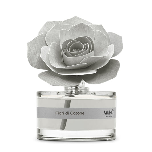 Profumatore d'ambiente Muhà Rosa Diffuser Fiori di Cotone in boccetta di vetro trasparente con essenza grigio chiaro, etichetta argento e diffusore artigianale a forma di rosa in legno grigio perla, Tutto Chic.