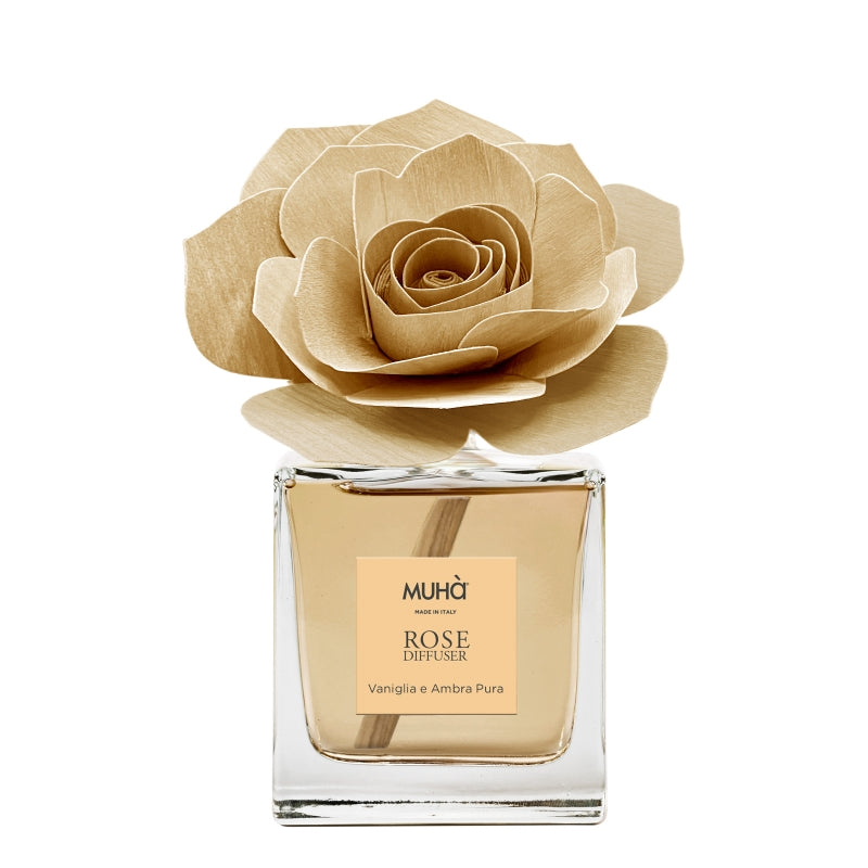 Profumatore d'ambiente Muhà Rose Diffuser Vaniglia e Ambra Pura in flacone squadrato di vetro trasparente con essenza dorata, etichetta centrale quadrata e diffusore artigianale a forma di rosa in legno ocra chiaro, Tutto Chic.