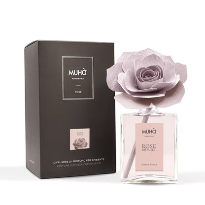 Profumatore d'ambiente Muhà Rose Diffuser Ambra Antica in flacone grande squadrato di vetro trasparente con essenza rosata, etichetta verticale rosa cipria e diffusore artigianale a forma di rosa in legno color rosa antico desaturato, Tutto Chic.