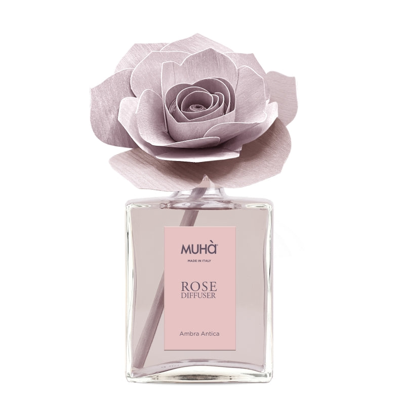 Profumatore d'ambiente Muhà Rose Diffuser Ambra Antica in flacone grande squadrato di vetro trasparente con essenza rosata, etichetta verticale rosa cipria e diffusore artigianale a forma di rosa in legno color rosa antico desaturato, Tutto Chic.