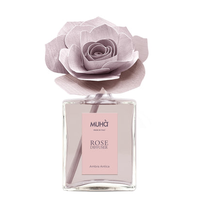 Profumatore d'ambiente Muhà Rose Diffuser Ambra Antica in flacone grande squadrato di vetro trasparente con essenza rosata, etichetta verticale rosa cipria e diffusore artigianale a forma di rosa in legno color rosa antico desaturato, Tutto Chic.