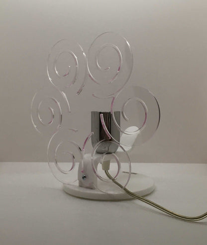 Lampada da tavolo in metacrilato trasparente con profilo viola soft. Base e supporto in metacrilato bianco e portalampadina in metallo cromato. Si può applicare qualsiasi lampadina con attacco filettato E 27 (non inclusa). Dimensioni: cm 23 x 23 x 15 p. In negozio e online su tuttochic.live