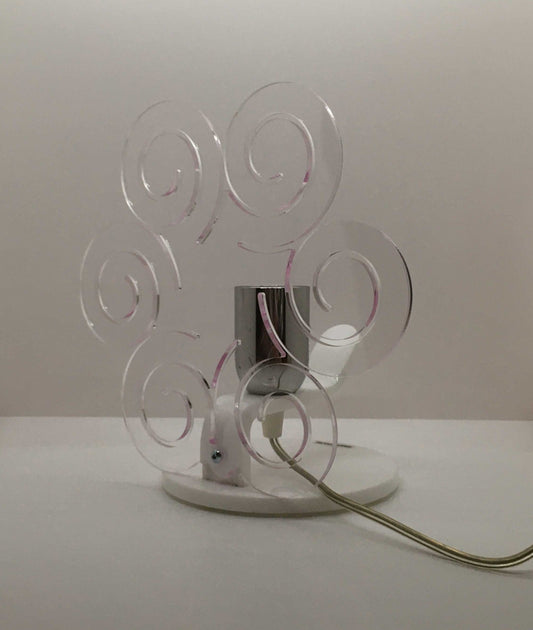 Lampada da tavolo in metacrilato trasparente con profilo viola soft. Base e supporto in metacrilato bianco e portalampadina in metallo cromato. Si può applicare qualsiasi lampadina con attacco filettato E 27 (non inclusa). Dimensioni: cm 23 x 23 x 15 p. In negozio e online su tuttochic.live