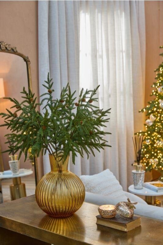 Composizione di rami verdi Cryptomeria EDG all'interno di un elegante vaso in vetro ambrato su un tavolo in legno in un salone accogliente.