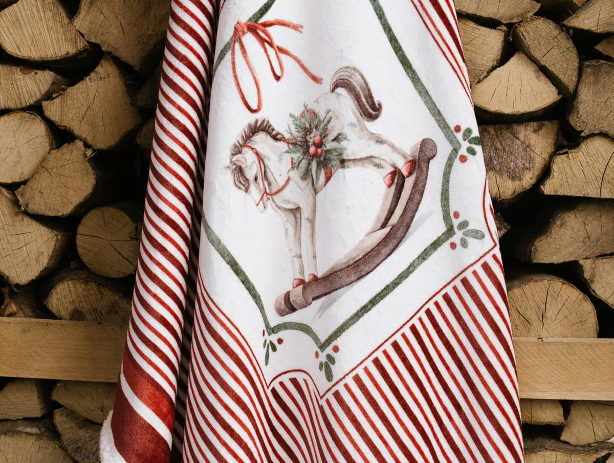 Esclusivo plaid natalizio Magic Noel di Nuvole di Stoffa ripiegato nella sua scatola regalo rigida, motivo a righe bianche e rosse con cavallo a dondolo, Tutto Chic.